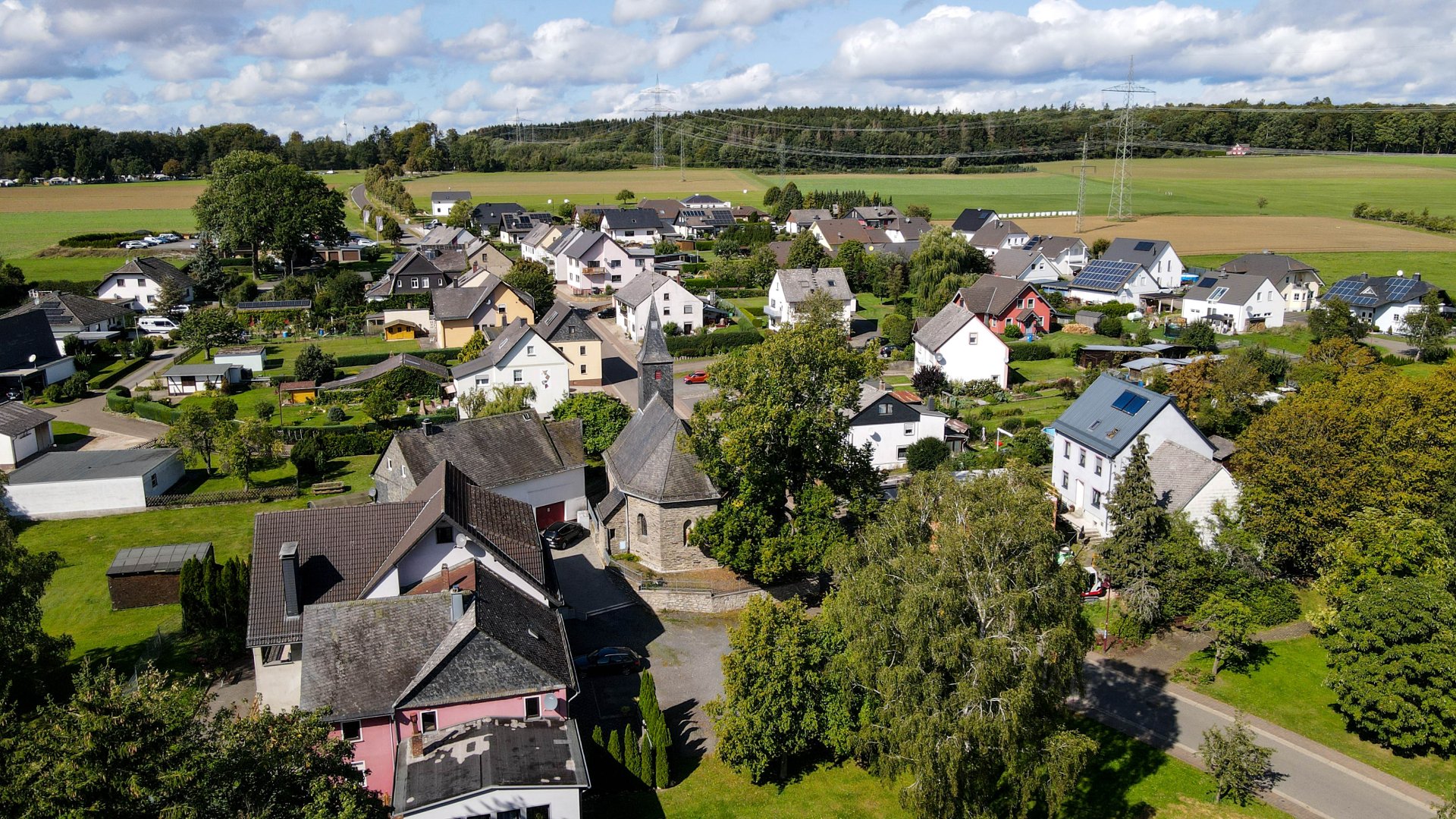 Ortsansicht Erbach mit der Kirche im Dorfmittelpunkt. Blick auf den Campingplatz am Waldrand bei schönem Wetter