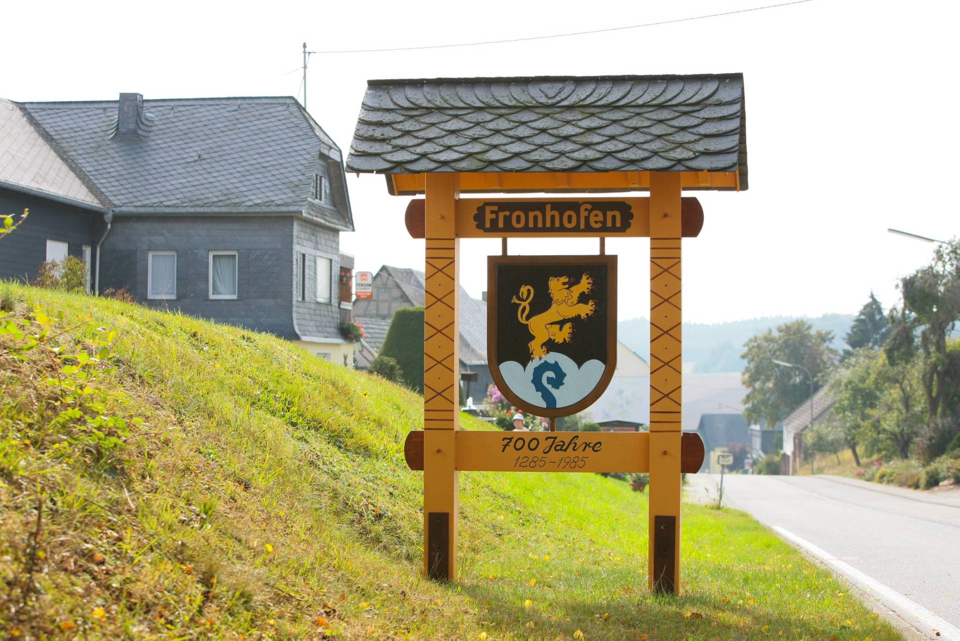 Holzschild am Ortseingang von Fronhofen zur Erinnerung an die 700-Jahr-Feier mit dem Ortswappen