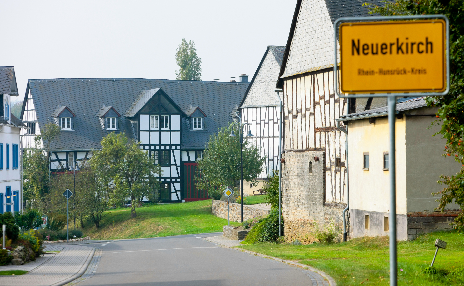 Häuseransicht mit Ortsschild im Vordergrund, bei sonnigem Wetter