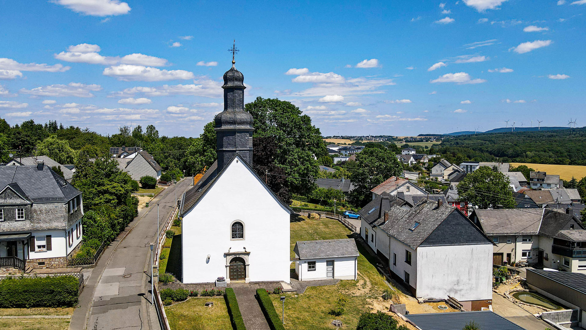 Ortsansicht von Riesweiler mit Kirche Häuseransicht mit der evangelischen Kirche im Vordergrund bei Sonnenschein und blauem Himmel von der Ortsgemeinde Riesweiler