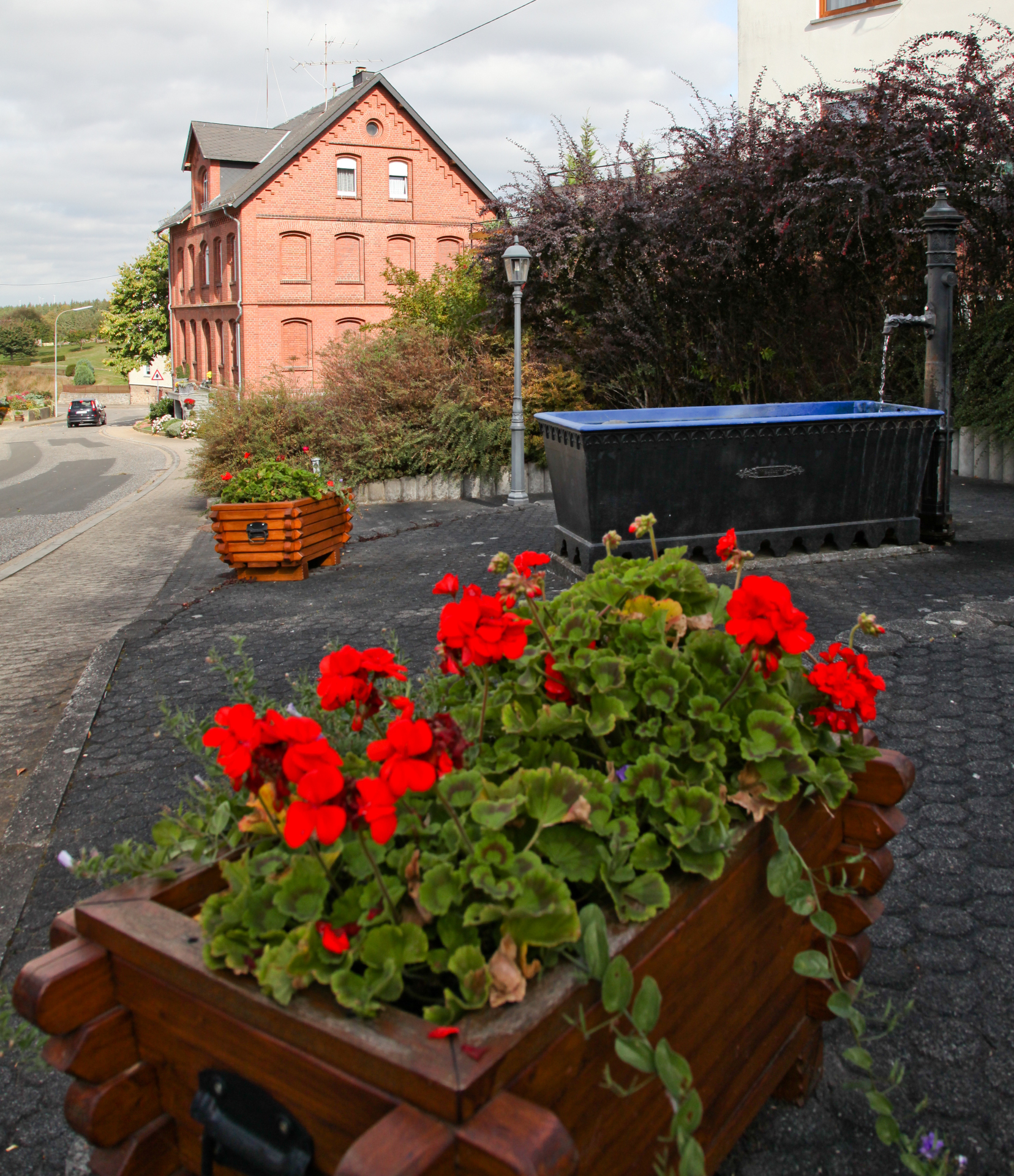 Dorfmitte der Ortsgemeinde Wahlbach mit roten Geranien im Blumenkasten und dem Dorfbrunnen