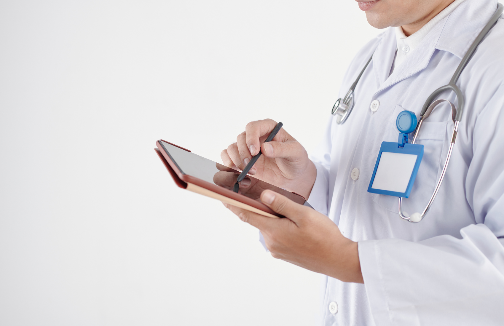 Arzt mit weißem Kittel und Stethoskop schreibt auf einem Tablet mit einem Stift.