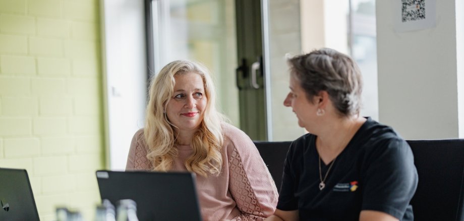 Zwei Mitarbeiterinnen sitzen am Laptop und reden miteinander
