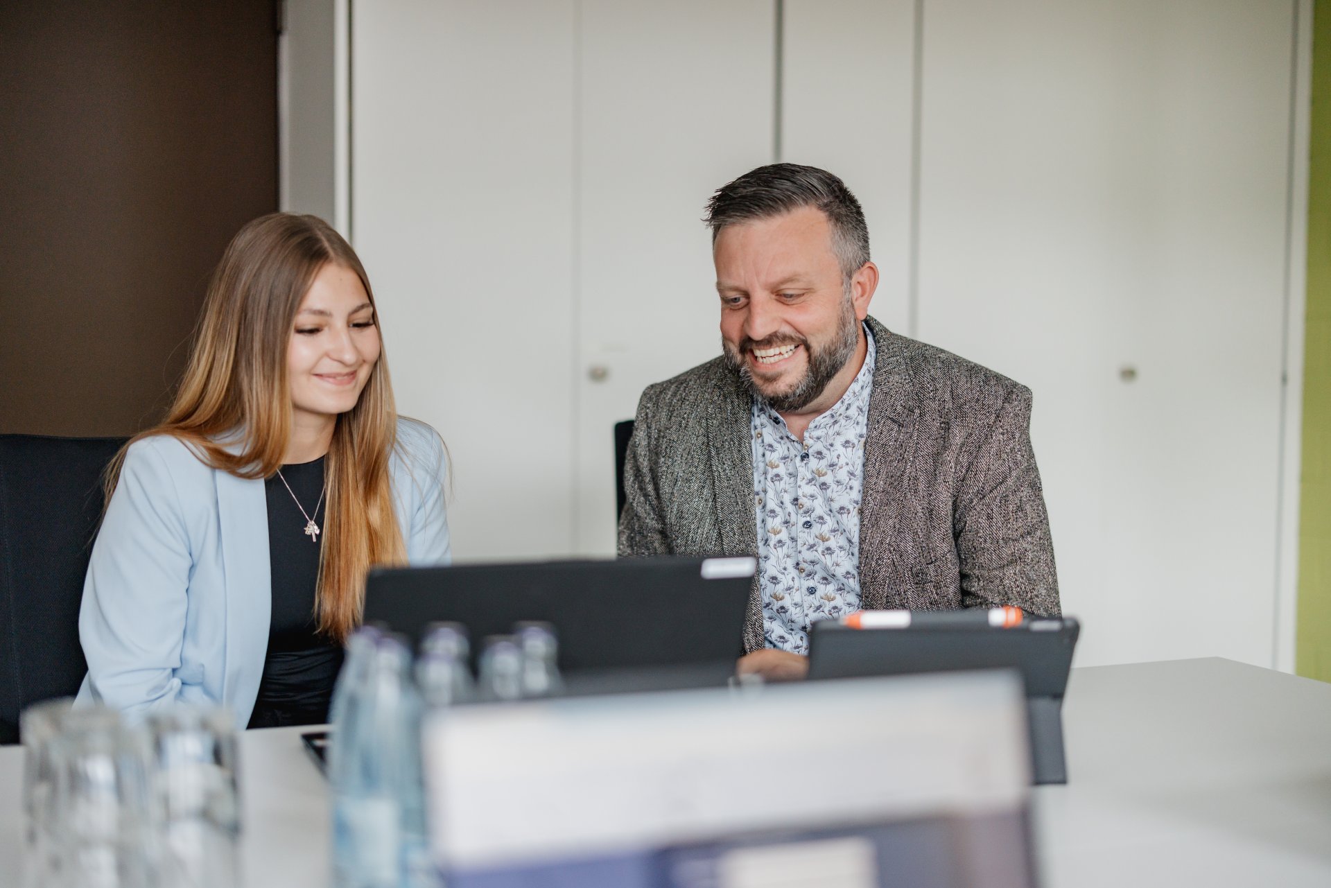Eine Mitarbeiterin und ein Mitarbeiter sitzen zusammen am Laptop und besprechen etwas