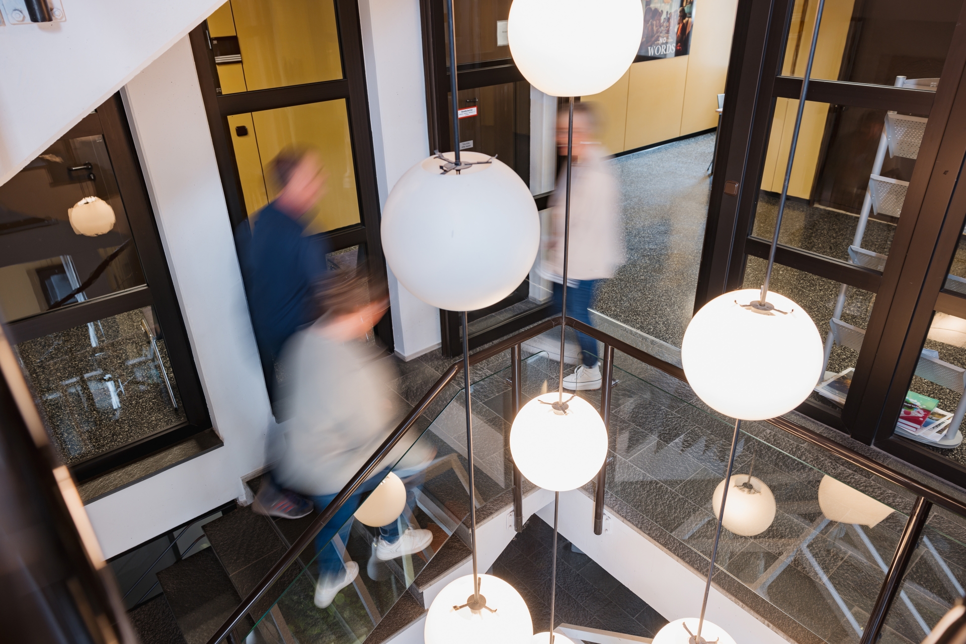 Zwei Personen laufen eine Treppe hoch, eine andere Person runter. Sie treffen sich in der Mitte.