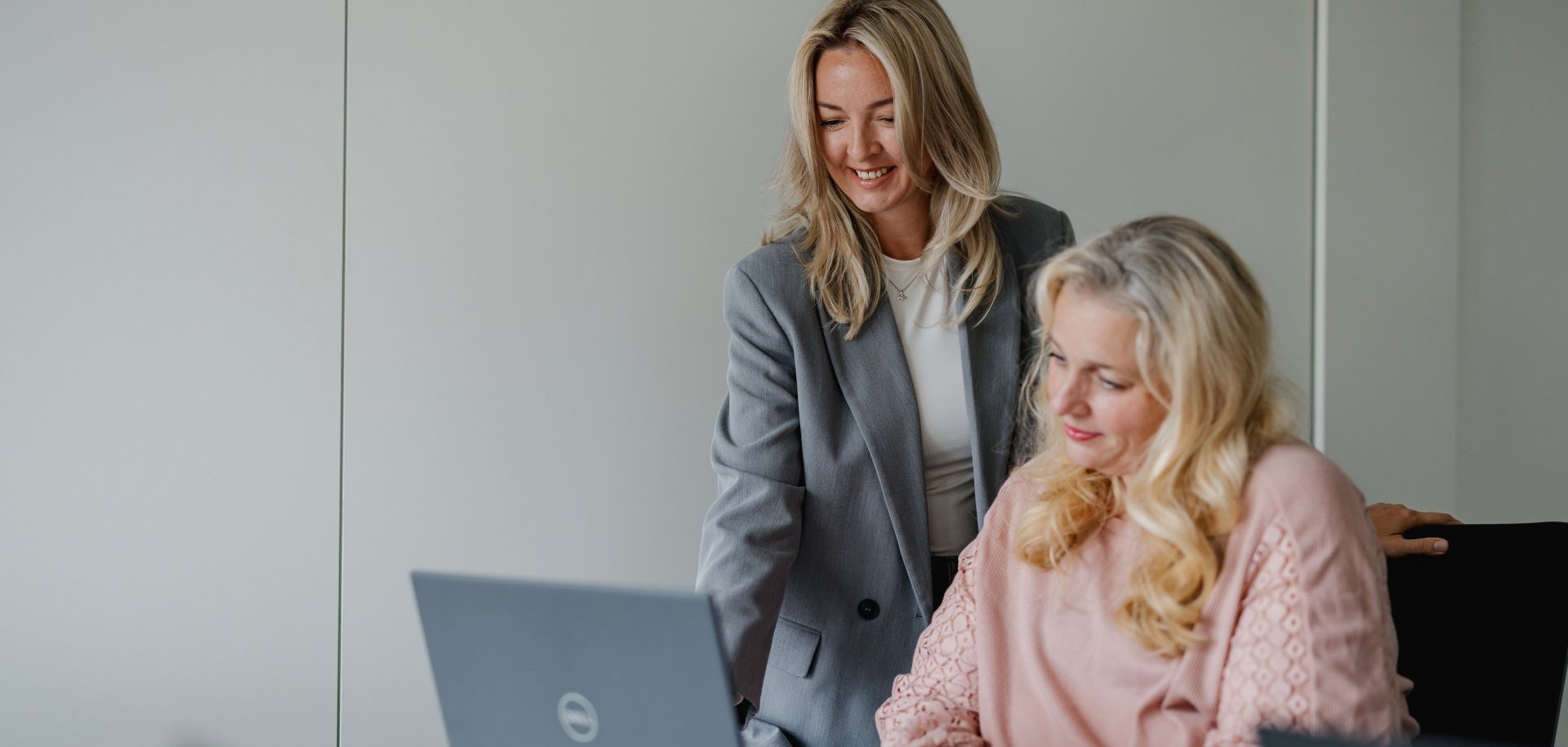 Zwei Mitarbeitende sitzen vor einem Laptop und begutachten den Inhalt auf dem Bildschirm. SIe freuen sich. 