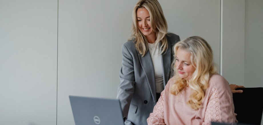 Zwei Mitarbeitende sitzen vor einem Laptop und begutachten den Inhalt auf dem Bildschirm. SIe freuen sich. 