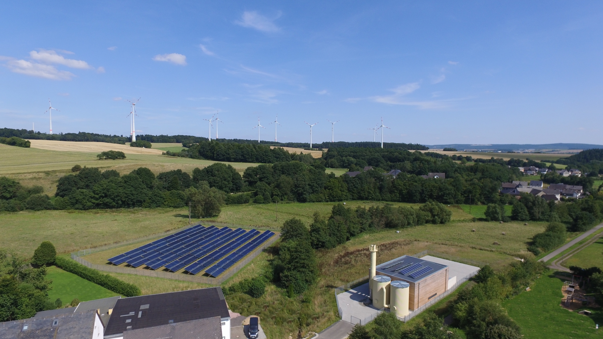 Nahwärme aus regenerativen Energiequellen. Man sieht Windräder und Freiflächen Photovoltaikanlagen im Hunsrück