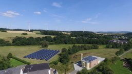 Nahwärme aus regenerativen Energiequellen. Man sieht Windräder und Freiflächen Photovoltaikanlagen im Hunsrück