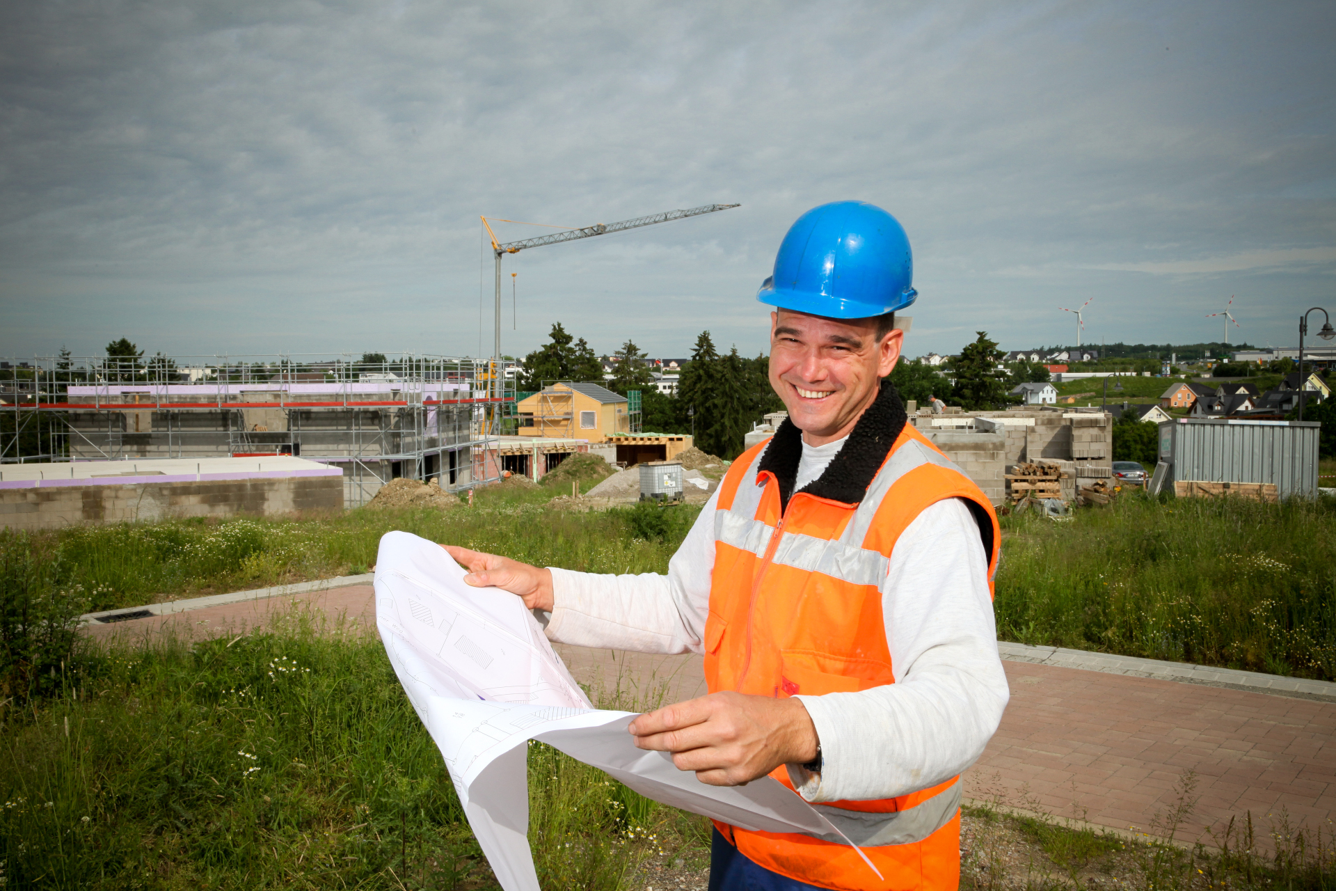 Ein Bauleitplaner steht mit einem aufgeklappten Plan vor einem Neubaugebiet