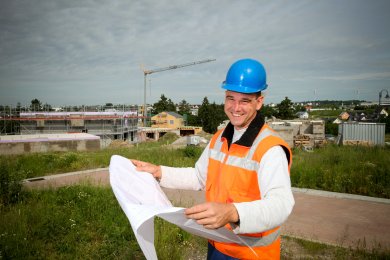 Ein Bauleitplaner steht mit einem aufgeklappten Plan vor einem Neubaugebiet