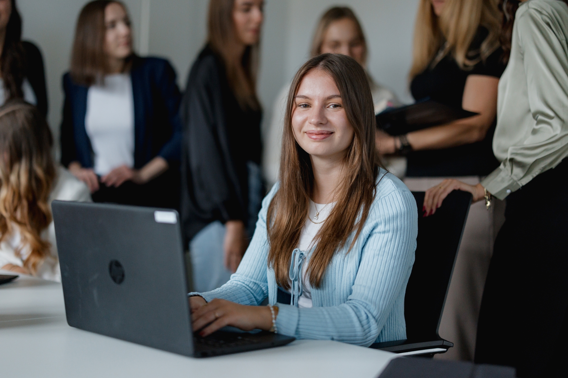 Auszubildene sitzt am Laptop, im Hintergrund unterhalten sich weitere Auszubildenden  miteinander