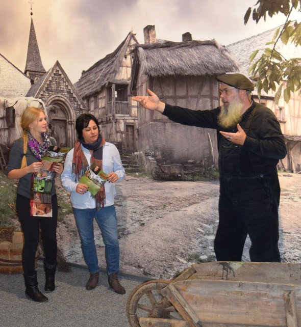 Ein Gästeführer präsentiert zwei Frauen die Geschichte Simmerns vor einer großen Leinwand.