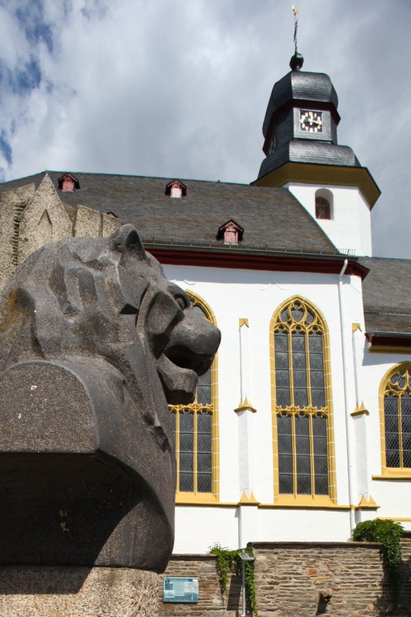 Die Stephanskirche in Simmern mit gelben Torbögen. Links sieht man einen Löwenkopf vor der Kirche