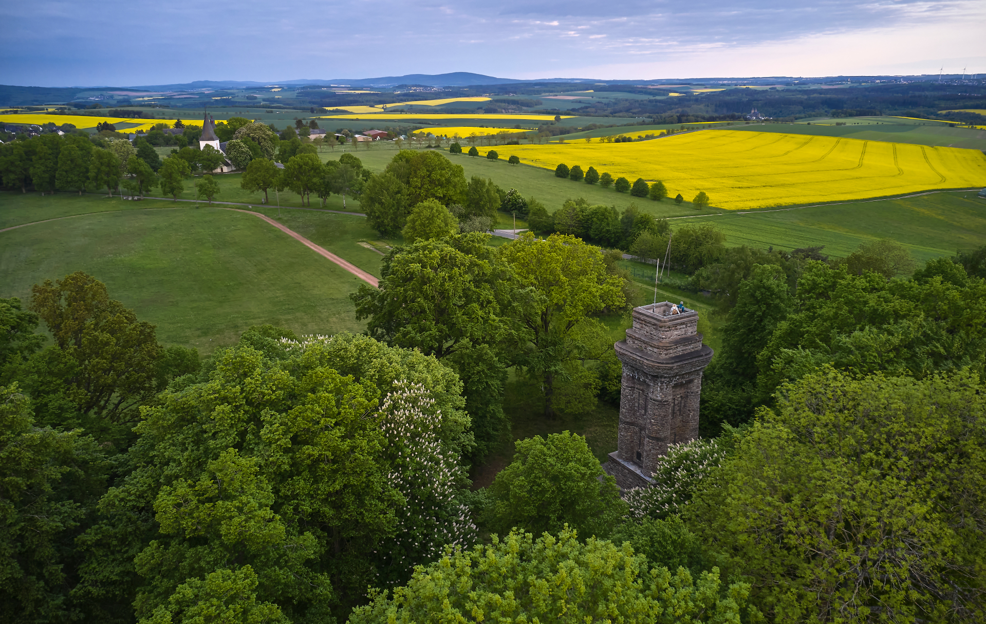 Drohnenaufnahme vom Bismarckturm in der Wanderregion Hunsrück. Im Hintergrund sieht man ein Rapsfeld
