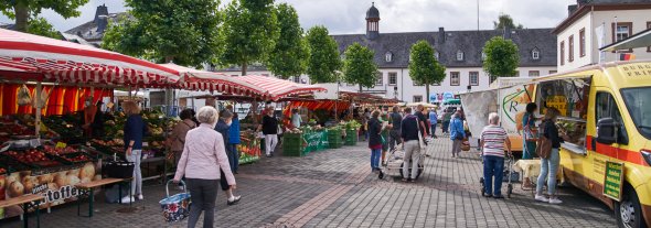 Wochenmarkt in Simmern mit einigen Personen, die unterschiedlichen Ständen stehen und einkaufen.
