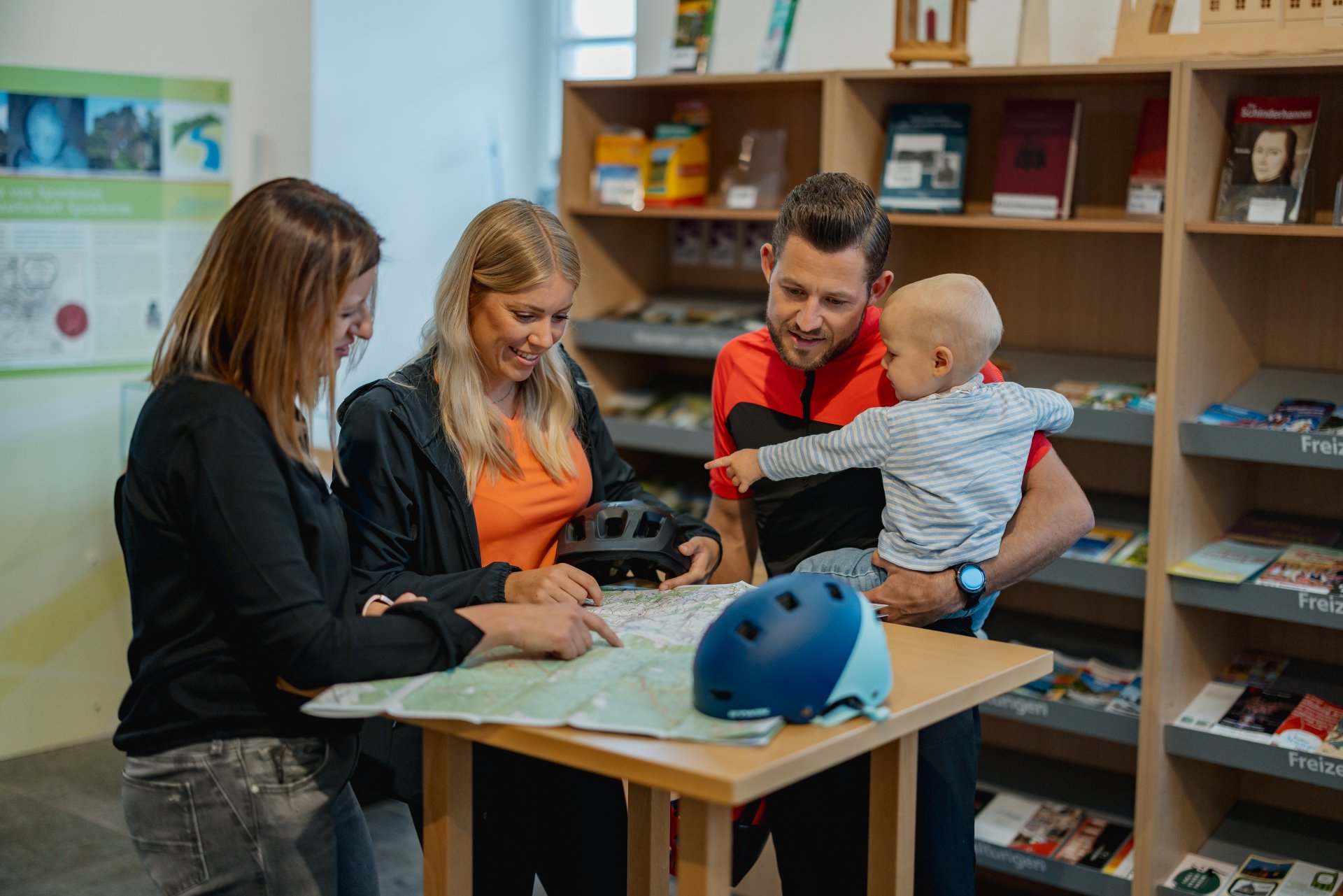 Beratungssituation in der Tourist-Information Simmern mit einer Mitarbeiterin und einer Familie mit Kleinkind