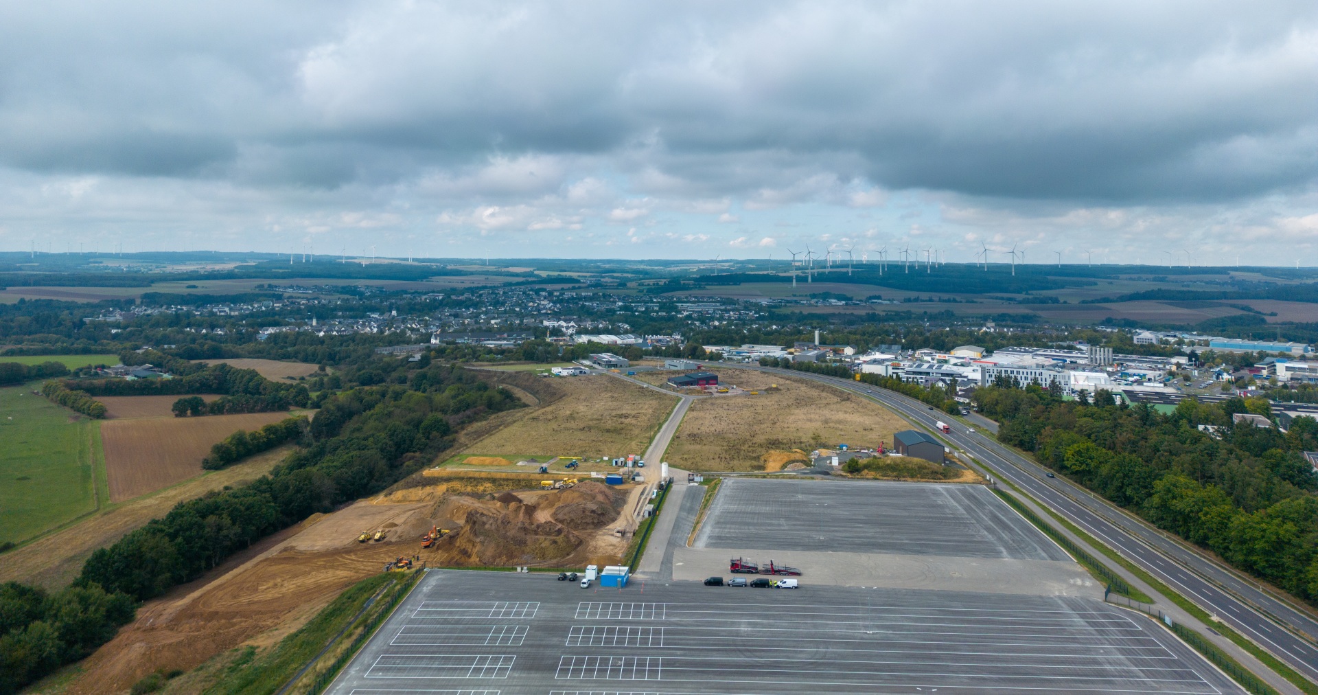 Luftaufnahme des Gewerbe- und Industriegebiets mit Gewerbe- und Industriegrundstücken im Industriepark West Simmern in der Verbandsgemeinde Simmern-Rheinböllen sowie umliegenden Feldern und der Stadt Simmern im Hintergrund.