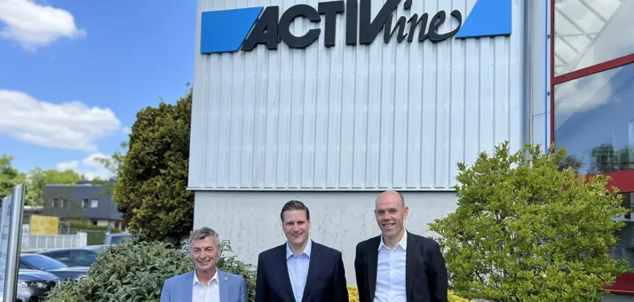 Drei Personen stehen vor dem Firmengebäude mit dem sichtbaren Schriftzug „ACTIVline“, umgeben von Pflanzen und Fassadenelementen.