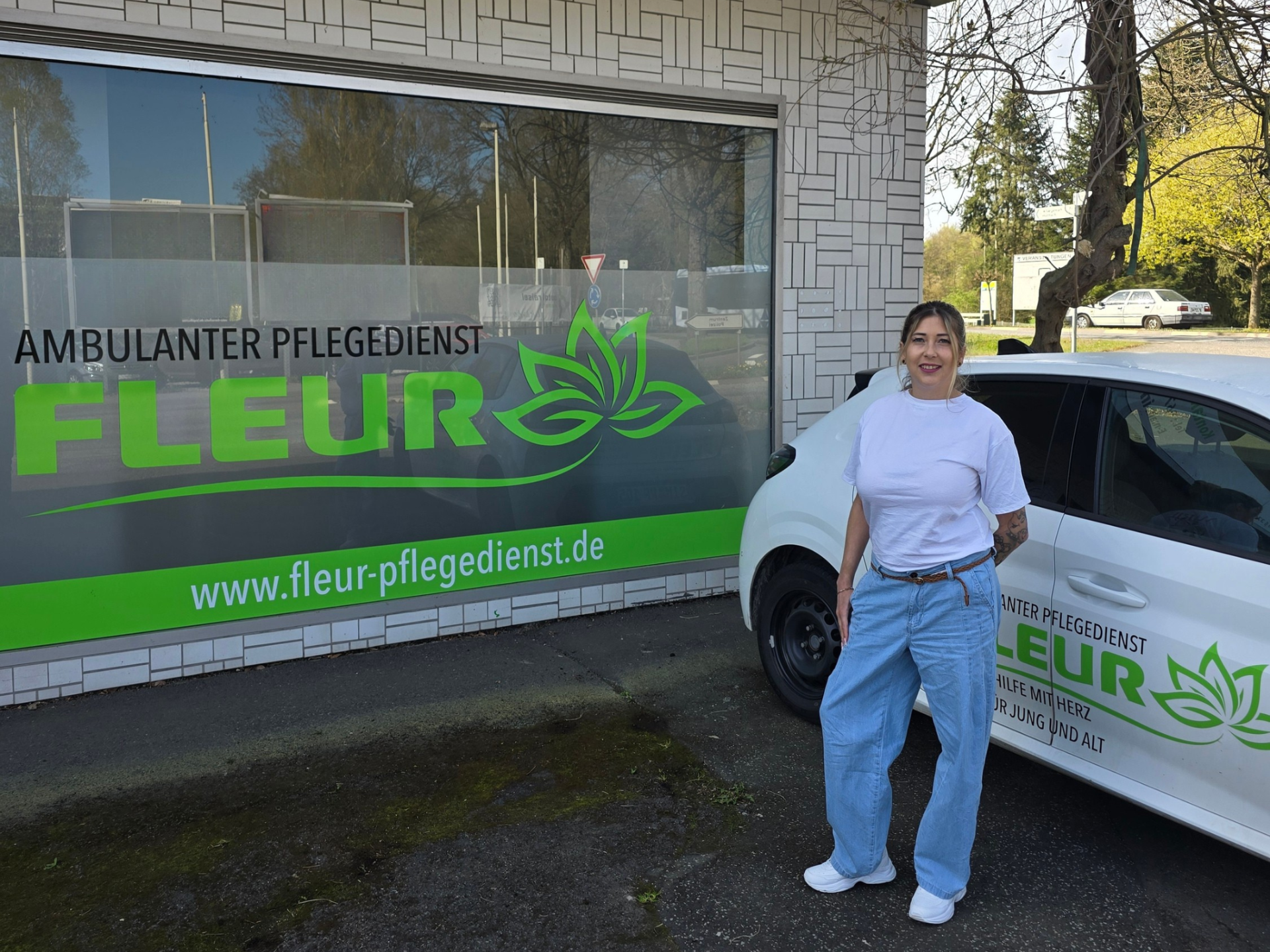 Inhaberin und Pflegedienstleiterin Kristina Baumgarten steht vor Firmengebäude von Ambulanter Pflegedienst Fleur GmbH, neben Firmenauto und Schaufenster.
