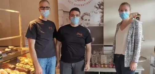 Unternehmensbesuch in der Bäckerei Dhein in Argenthal, gezeigt wird der Verkaufsbereich mit Backwaren-Auslage sowie drei Personen mit Mund-Nasen-Schutz vor einem Banner zum 160-jährigen Jubiläum des Familienbetriebs.