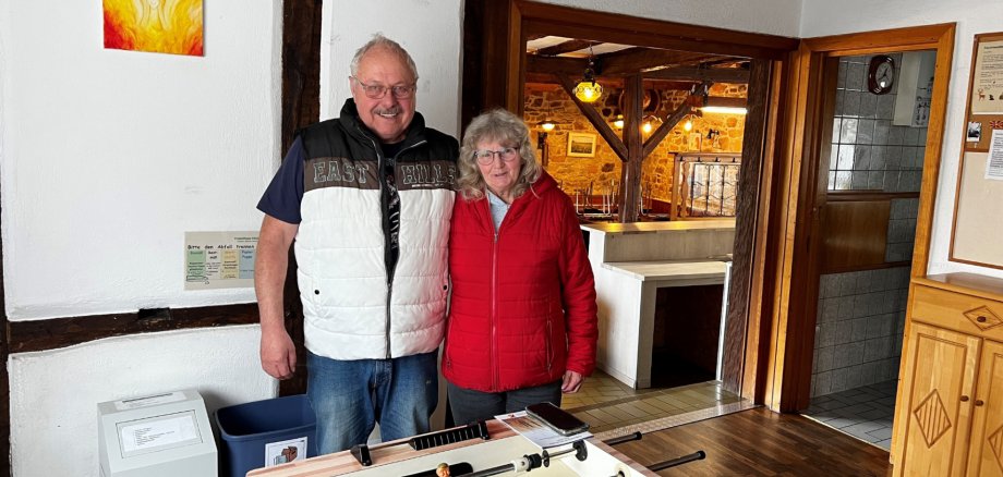 Fotos - Freizeithaus Engel - Foto Zwei Personen (Dörthe Kauth, Siegfried Kauth) stehen lächelnd in einem gemütlichen Raum neben einem Tischfußballtisch, Holzbalken sichtbar. Im Freizeithaus Engel im Stadtteil Kleinweidelbach von der Stadt Rheinböllen im Hunsrück.