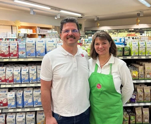 Zwei Personen stehen in einem Lebensmittelmarkt vor Regalen mit verpackten Waren und Kühlthekenprodukten.