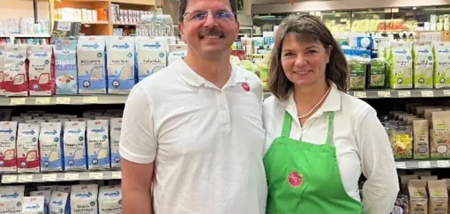 Zwei Personen stehen in einem Lebensmittelmarkt vor Regalen mit verpackten Waren und Kühlthekenprodukten.