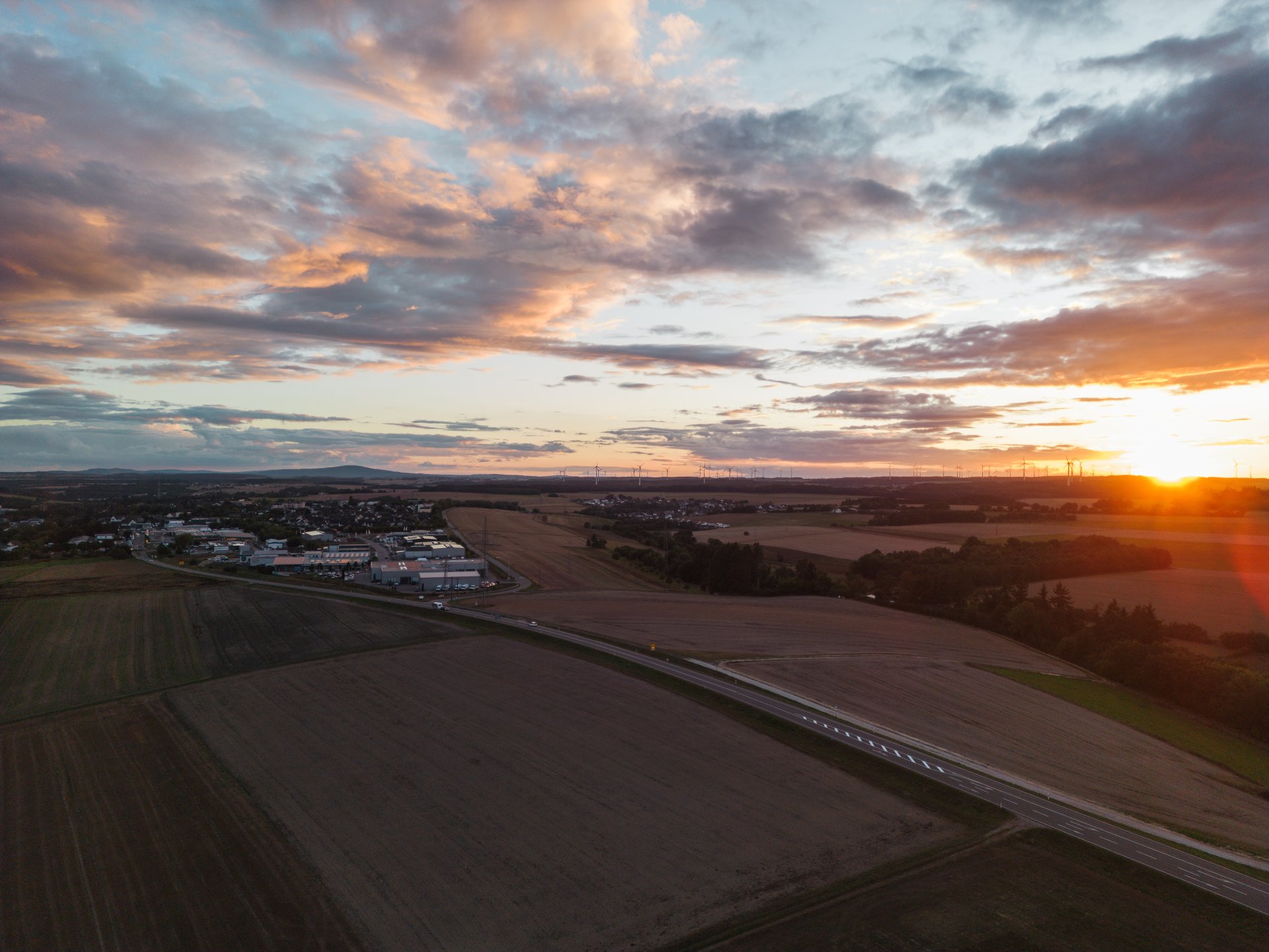 Luftaufnahme bei Sonnenuntergang mit Gewerbe- und Ortsbereichen sowie umliegenden Feldern in der Verbandsgemeinde Simmern-Rheinböllen im Rhein-Hunsrück-Kreis. Teile der Stadt Simmern im Hintergrund.
